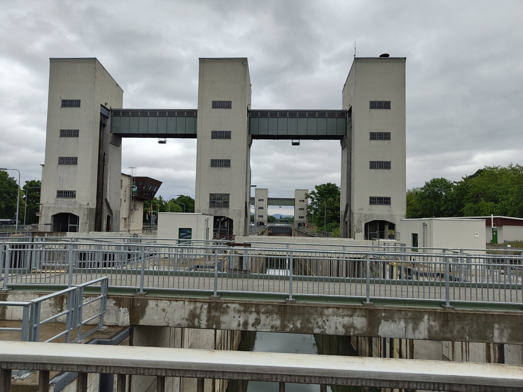 A series of tall, industrial-style structures stand over a canal, with bridges and railings connecting them under a cloudy sky.