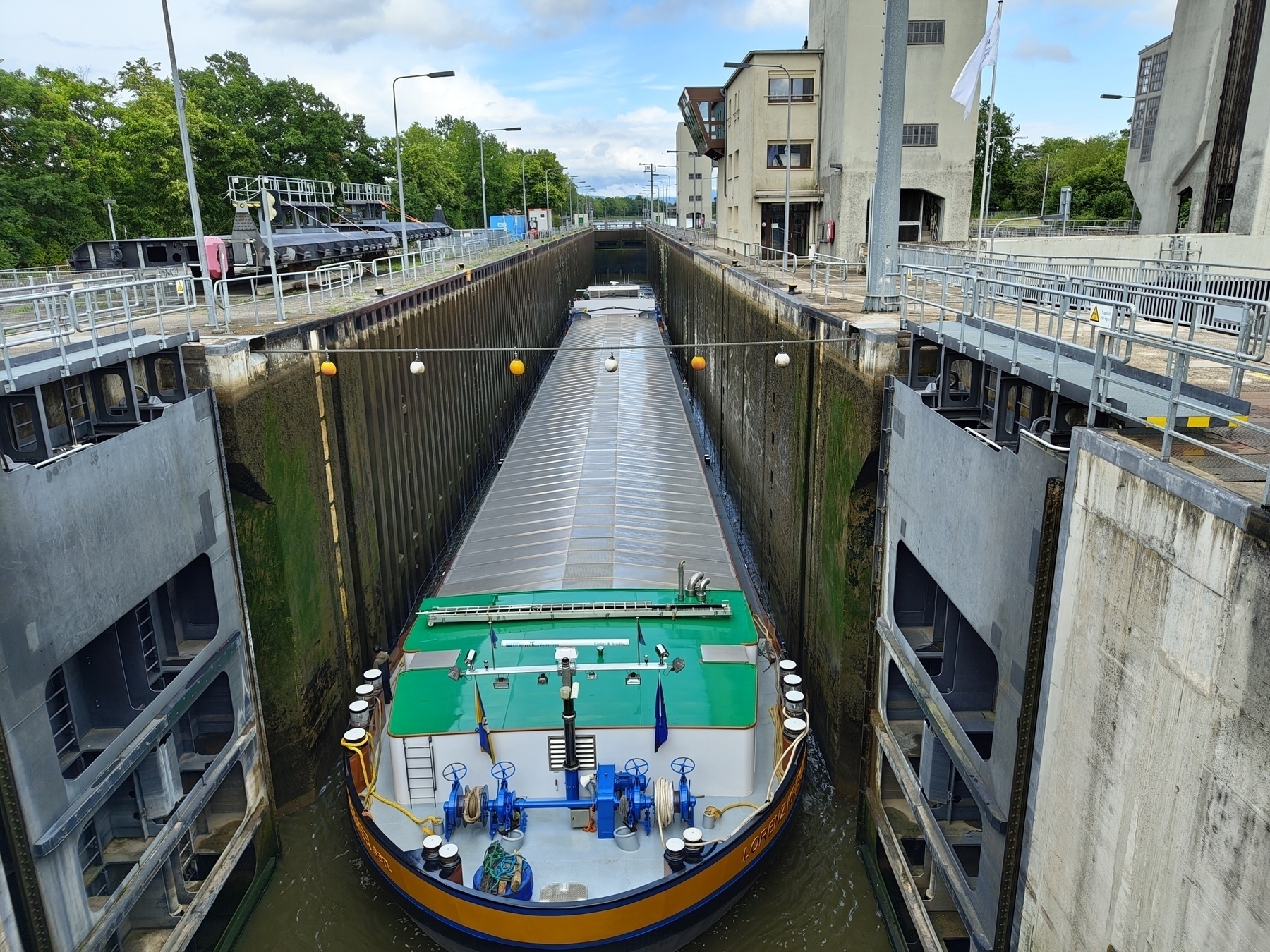 A barge is navigating through a canal lock surrounded by buildings and greenery.