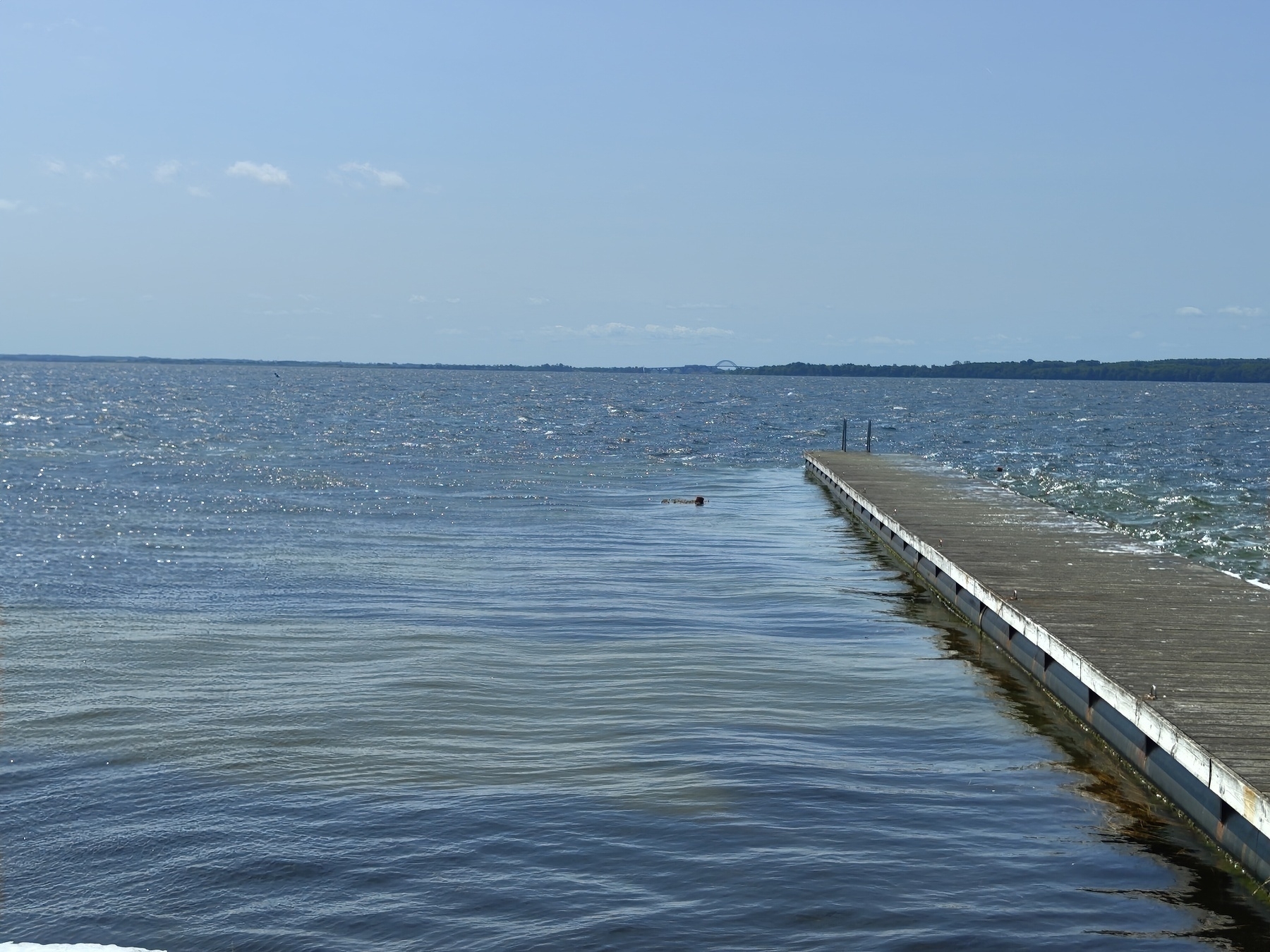 A long wooden pier extends into a calm, expansive body of water under a clear blue sky.