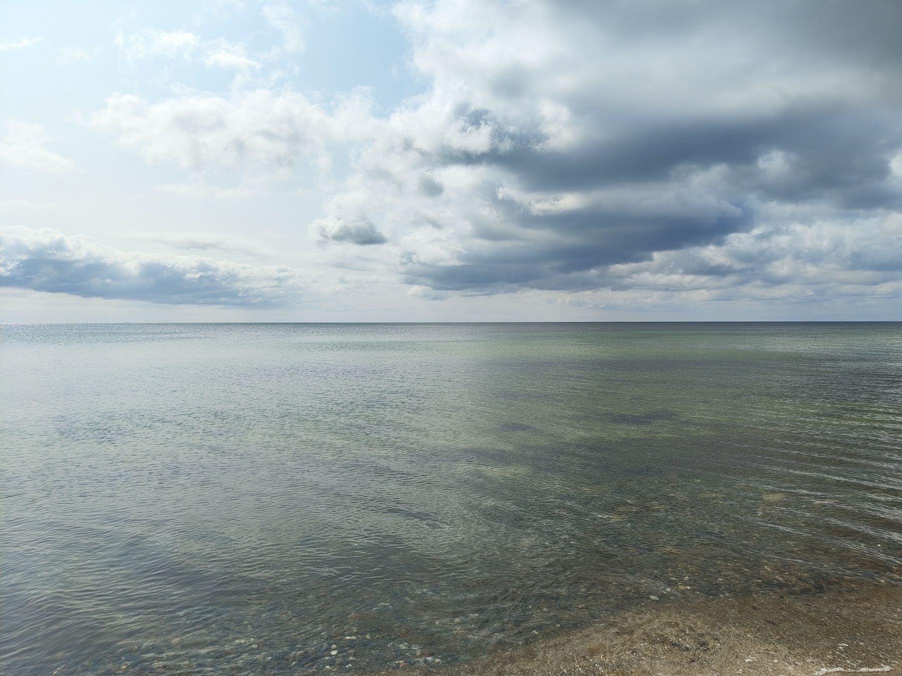A vast, calm ocean stretches under a partly cloudy sky, with gentle waves lapping at the shoreline.